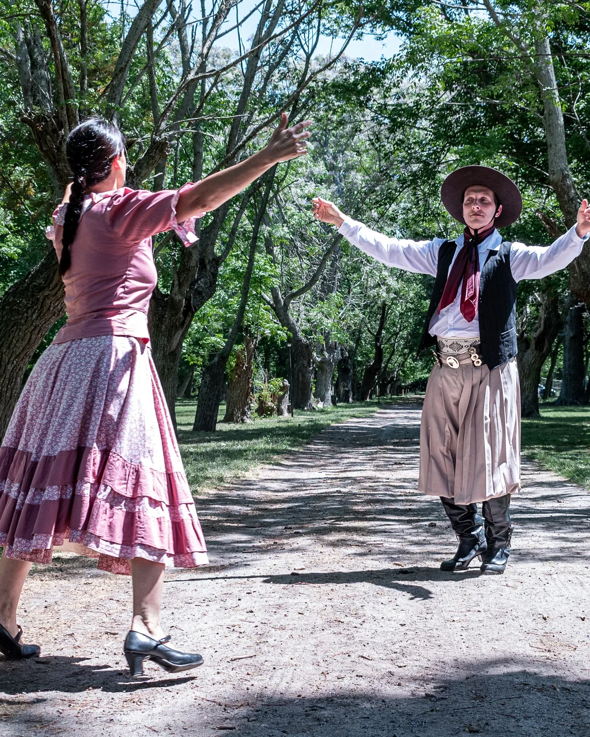 Two dancers in traditional gaucho and countryside dress mid-performance on a tree-lined path (representative photograph of an Argentine gaucho folk dance, not Señor Tango's own stage)
